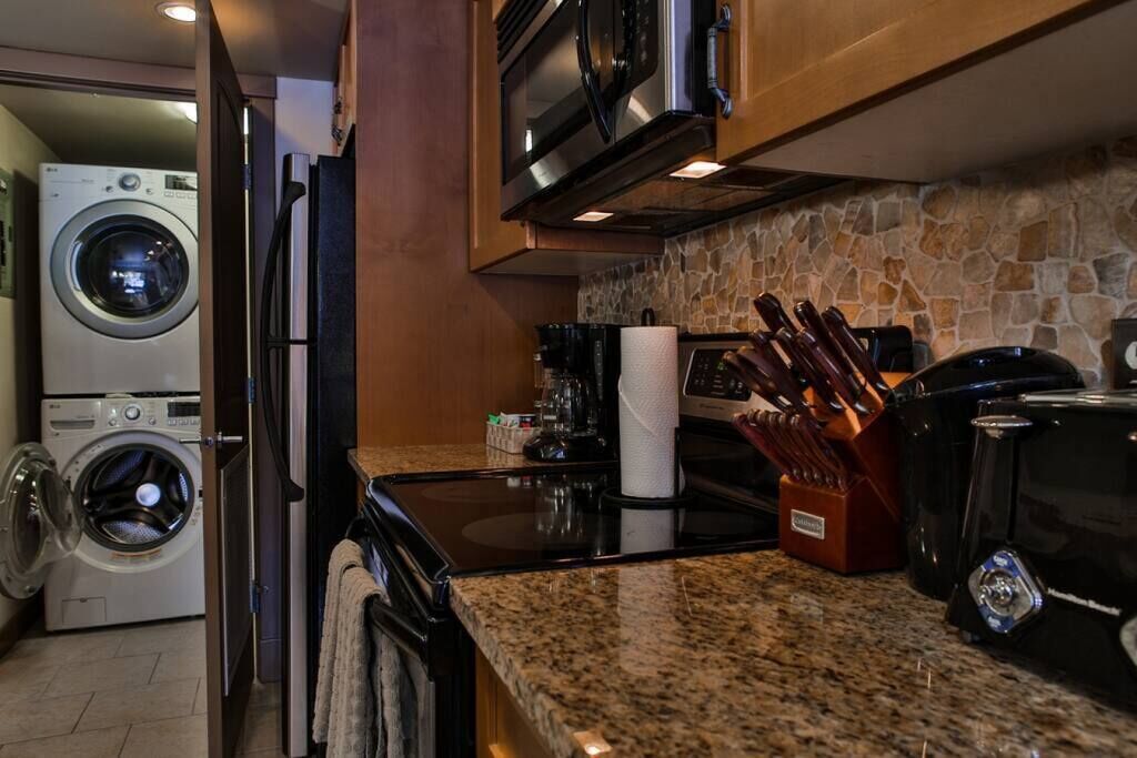 A compact kitchen with a washing machine, microwave, and granite countertop.