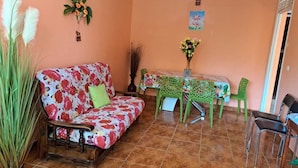 A room with a floral sofa, a dining table with chairs, and a ceiling fan.