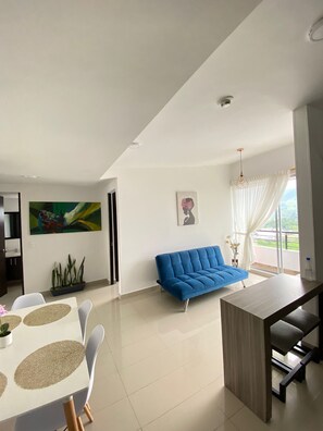 Una sala moderna con un sofá azul, una mesa de comedor con sillas y una zona de cocina.