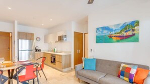 Et moderne køkken med køleskab, mikroovn og komfur. Der er et spiseområde med et bord og stole. En sofa med farverige puder er i opholdsstuen.