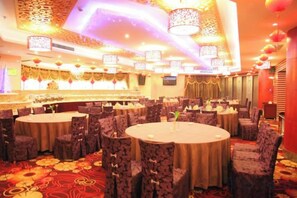 Un salón de banquetes con mesas redondas y sillas, una alfombra estampada y luminarias decorativas.