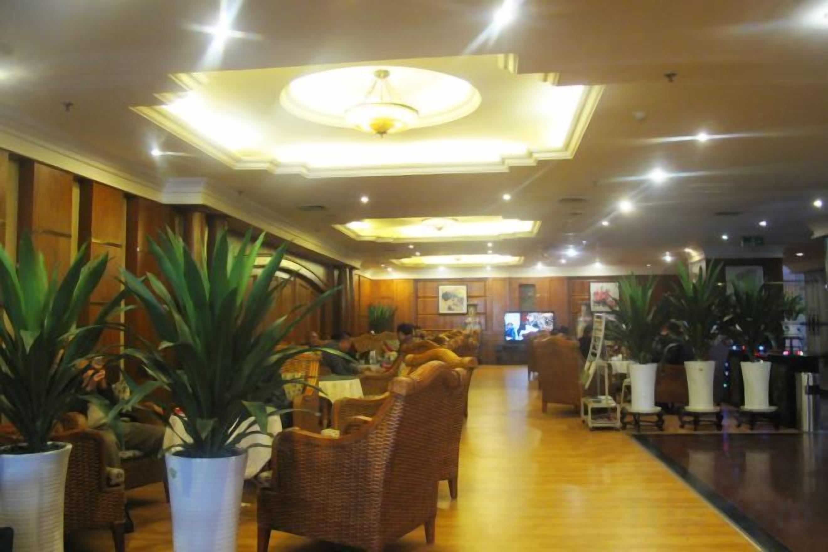 Eine Hotelhalle mit Korbmöbeln, Blumentöpfen und einer zentralen Leuchte.