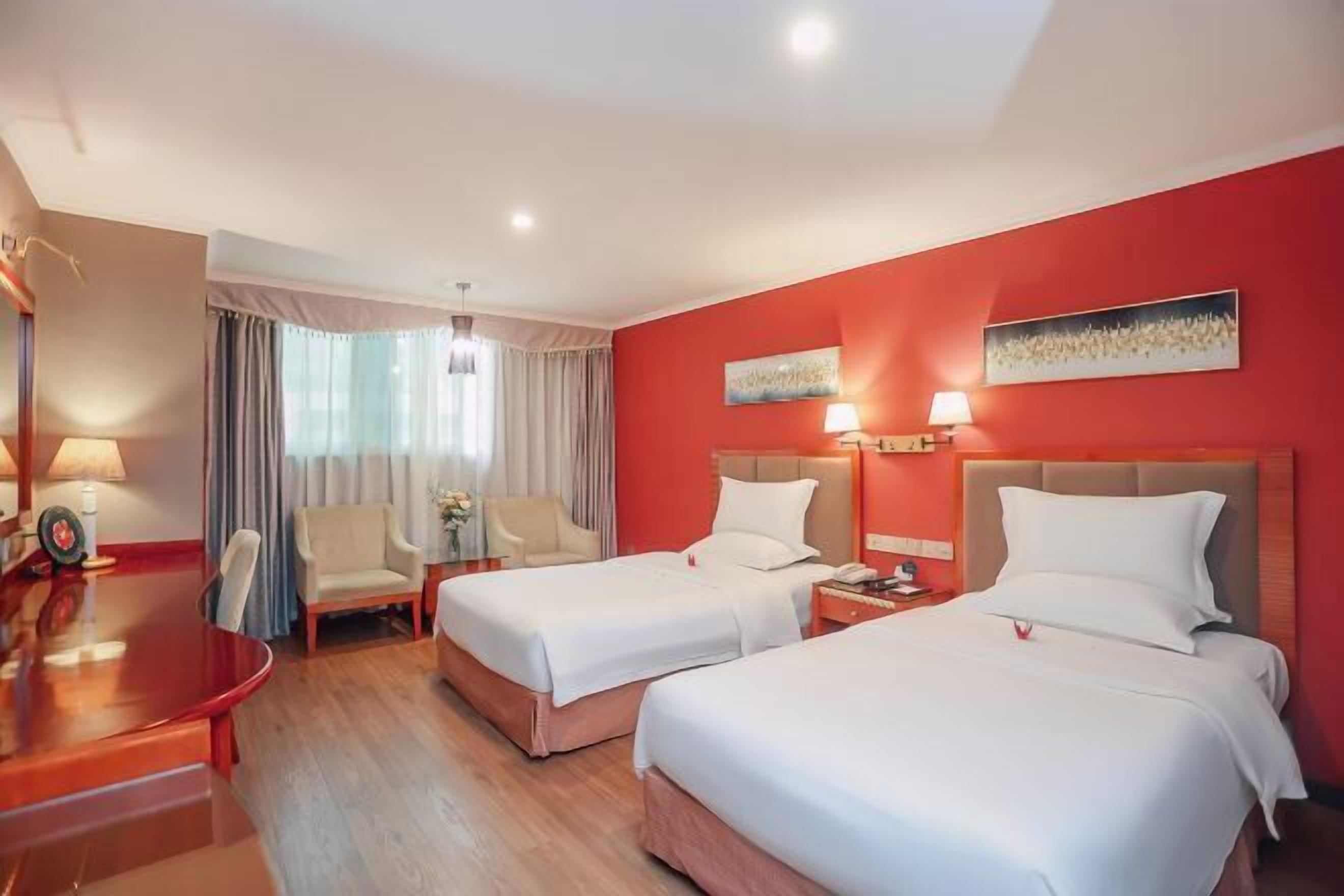 A hotel room with two beds, a desk, a chair, and a window with curtains.