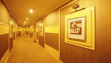 A hotel hallway with patterned carpet, wooden walls, and framed artwork.
