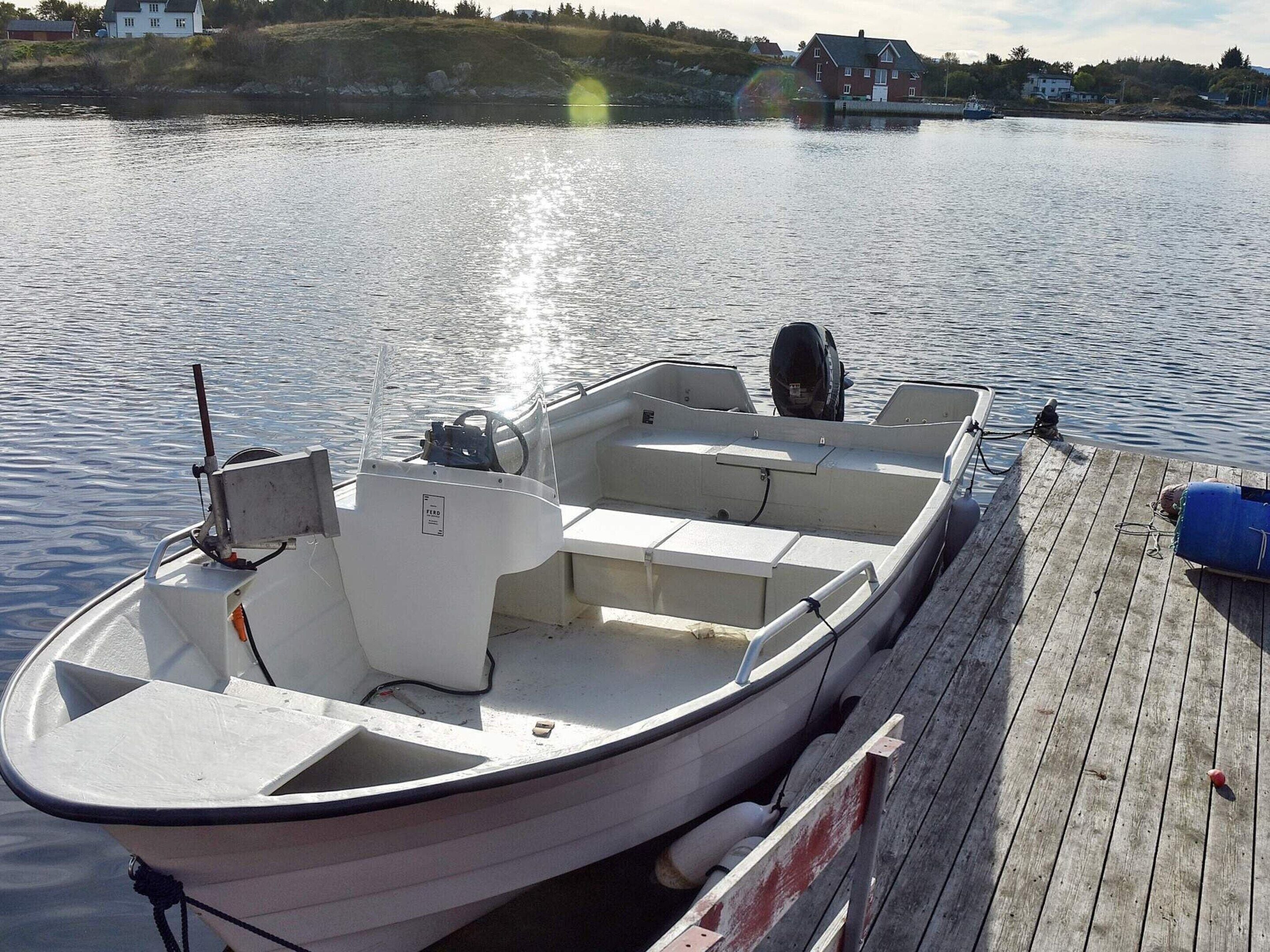 Un petit bateau à moteur blanc était amarré à un quai en bois, avec une étendue d’eau calme en arrière-plan.