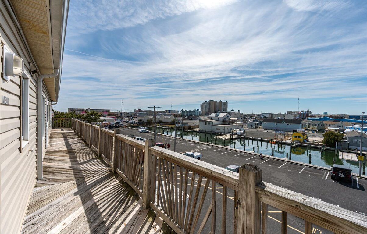 A wooden deck overlooking a marina with boats, a parking lot, and buildings in the background.