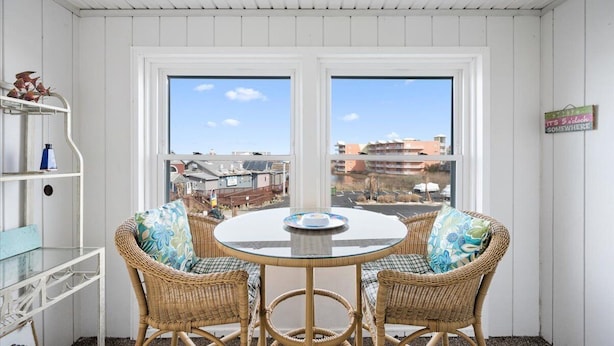 A room with a round glass table and wicker chairs, two windows with a view of buildings, and a white ceiling. - Great Midtown Location with Water Views! (Ocean City)