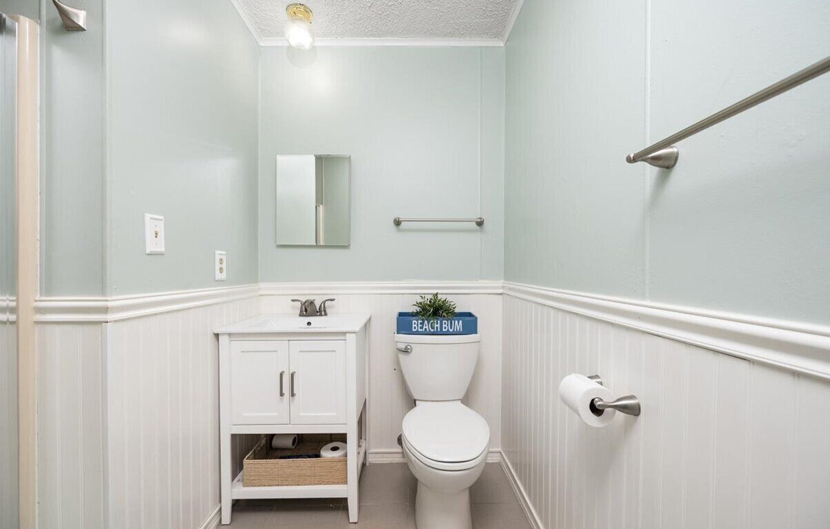 Un baño con inodoro, lavamanos, espejo y un perchero para toallas.