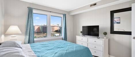 Une chambre à coucher avec un lit, une télévision, une commode et une fenêtre avec des rideaux.