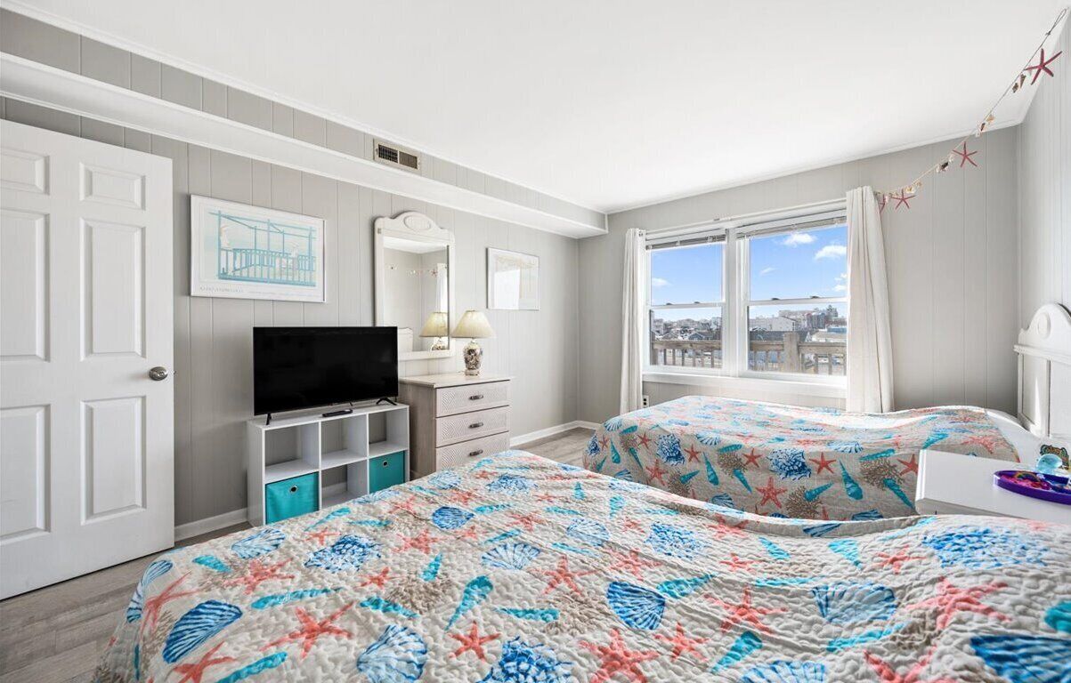 Un dormitorio con dos camas, televisión, cómoda y ventana con vista a la ciudad.