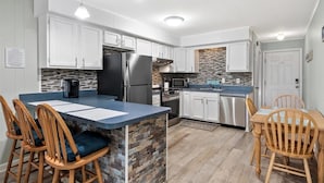 A modern kitchen with white cabinets, a granite island, and wooden chairs. - Great Midtown Location with Water Views! (Ocean City)