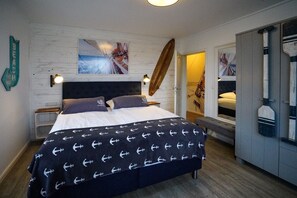 Quarto com cama, cabeceira de madeira, obra de arte na parede e um banquinho.
