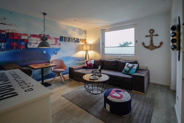 Uma sala de estar moderna com uma janela ampla, um sofá, uma mesa de centro e um mural de um navio de carga.
