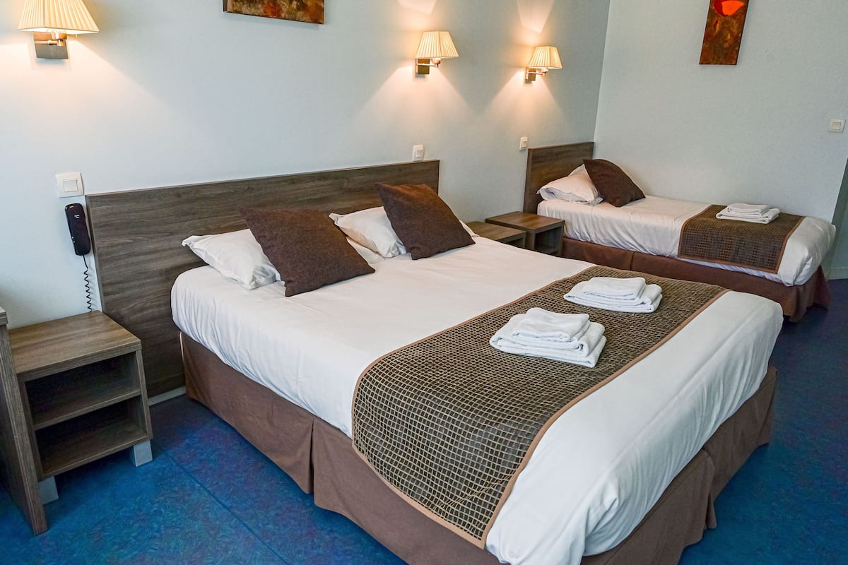 A hotel room with two beds, each with a headboard, bedside tables, and lamps.