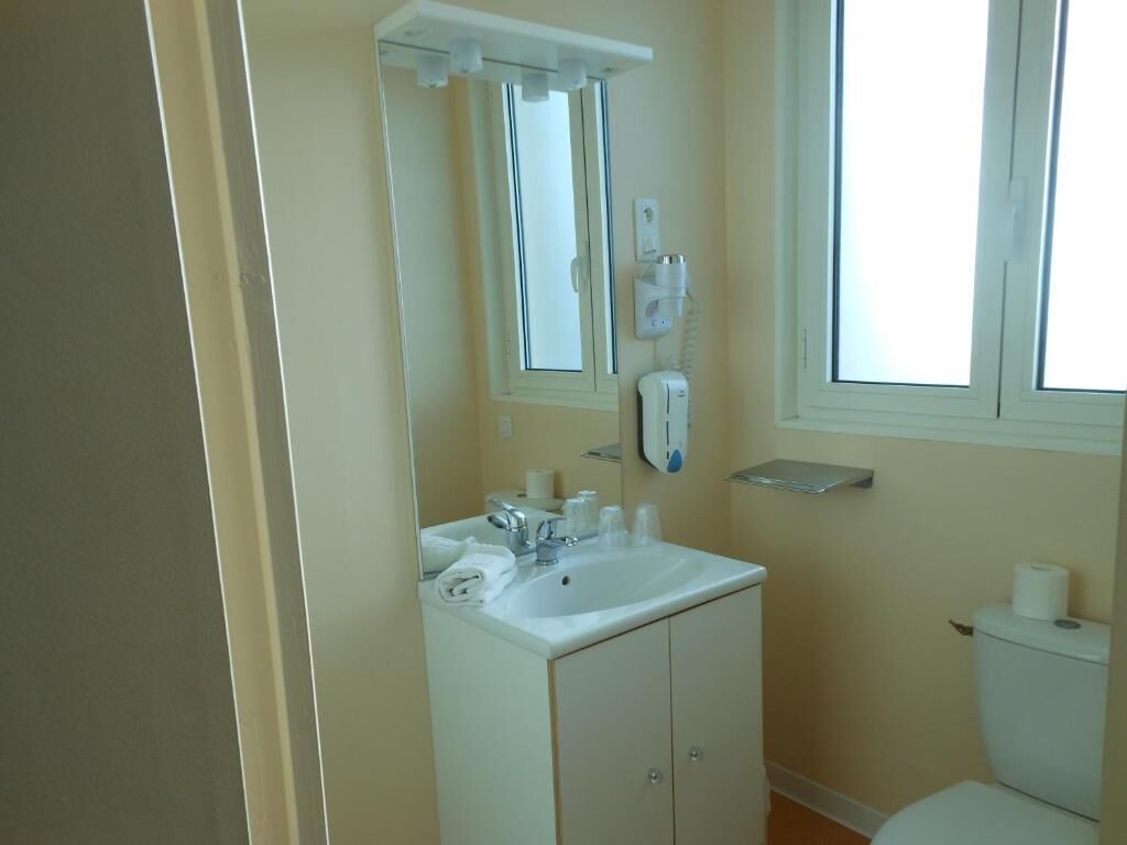 A bathroom with a white sink, mirror, and toilet. There is a window providing natural light and a towel rack above the sink.