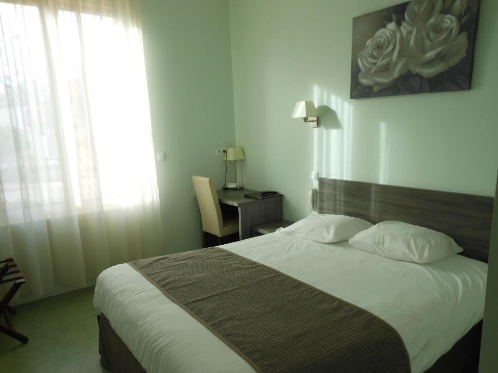 Habitación de hotel con cama, escritorio, silla, lámpara y un cuadro en la pared.