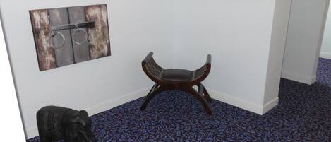 A room with a blue patterned carpet, a wooden chair, a wall-mounted artwork of a metal object, and a small elephant statue.