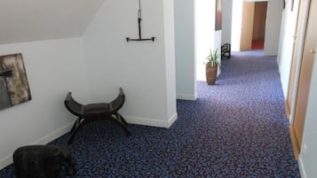 A hallway with a patterned carpet, a chair, a hanging light fixture, and a potted plant.