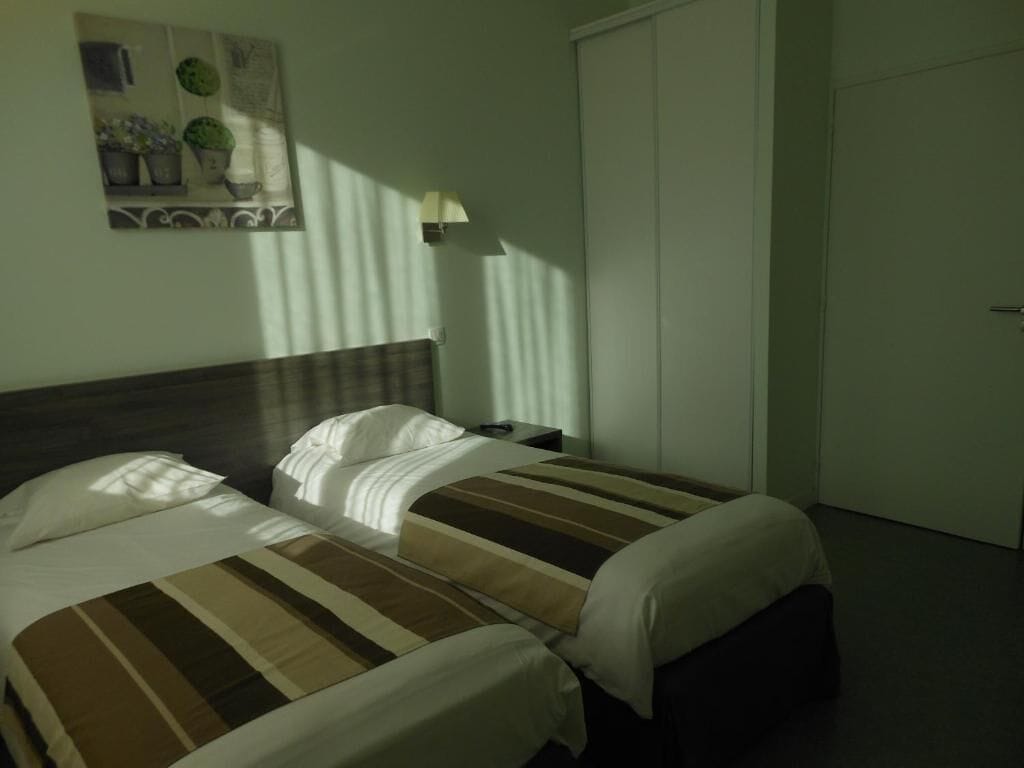 Una camera d'albergo con due letti, un comodino, una lampada e una porta.