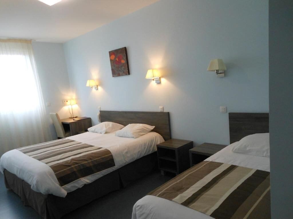 A hotel room with two beds, a nightstand, and wall-mounted lamps.