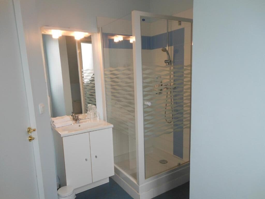 Un baño con tocador blanco, ducha con mampara de vidrio y espejo con luces arriba.