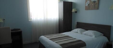 Quarto com cama, escrivaninha, guarda-roupa e janela com cortinas.
