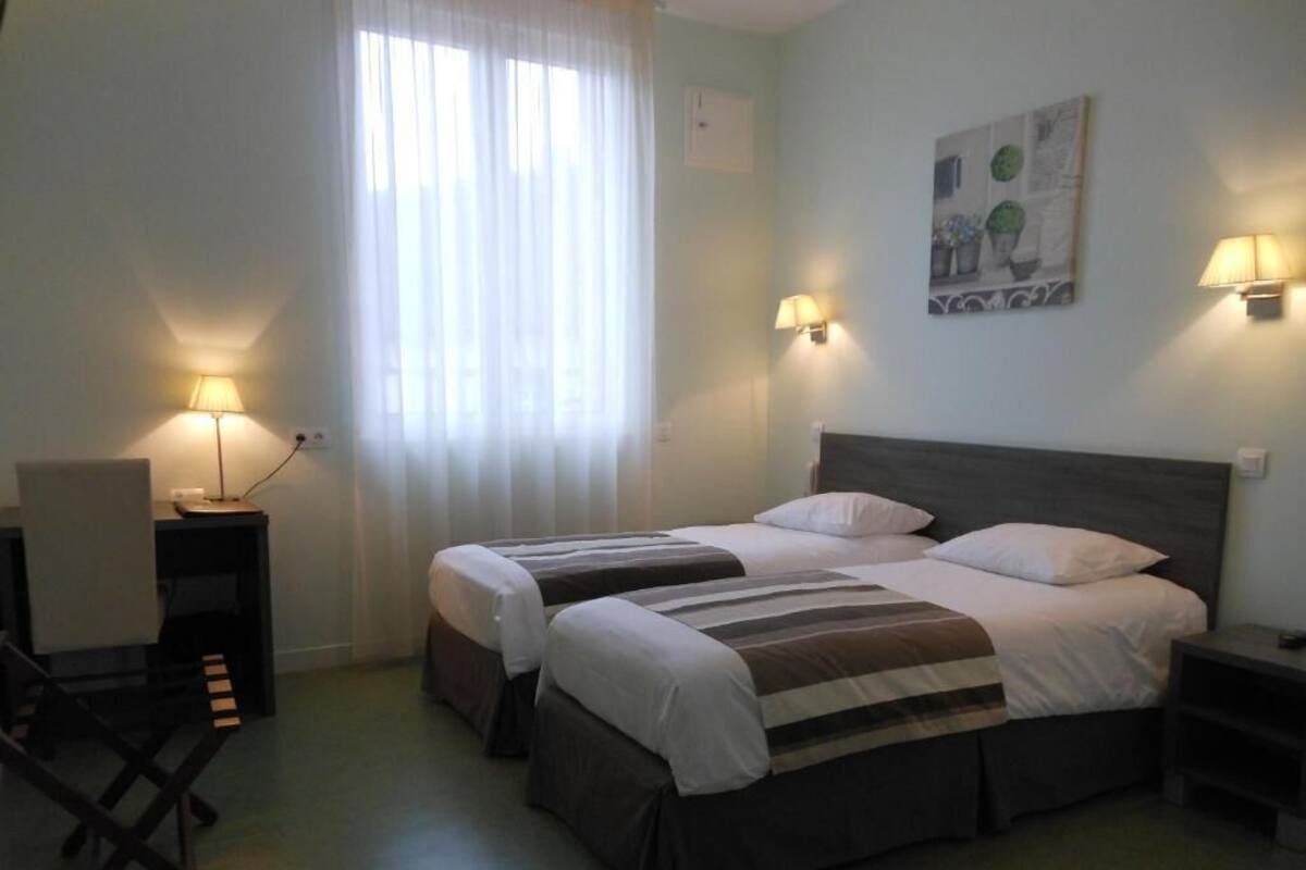A hotel room with two beds, a desk, and two wall-mounted lamps.