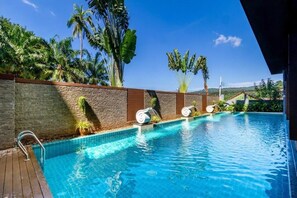 Relax by the serene pool surrounded by lush tropical vegetation and shaded lounge chairs.