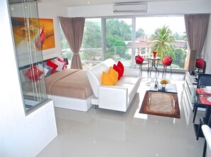 Relax in a spacious room with a large bed, sofa, and dining area, offering a view of palm trees and a nearby building.