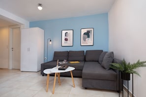 A modern living room with a grey sofa, a white table with wooden legs, and two framed abstract artworks on the wall.