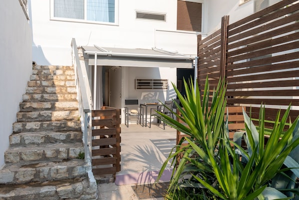 A courtyard with a stone staircase, a wooden gate, and a covered seating area with a table and chairs.