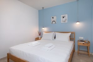 A neatly made bed with white linens and towels, a wooden headboard, and a bedside table with a book, glasses, and a cup.