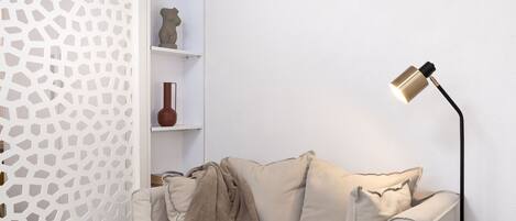 A modern living room with a beige sofa, a round black table with a yellow object, a floor lamp, and a white air conditioning unit on the wall.
