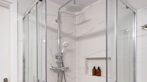 A glass-enclosed shower with a handheld showerhead and a fixed overhead showerhead.