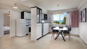 Une cuisine moderne avec des meubles blancs et un coin repas comprenant une table et des chaises. Une fenêtre offre une vue sur la mer.
