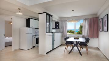 Een moderne keuken met witte kasten, een eethoek met een tafel en stoelen, en uitzicht op de oceaan door grote ramen.