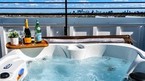 Ein Whirlpool mit Blick auf die Stadt, ein Holzboden mit Flaschen und Gläsern sowie ein Blumentopf.