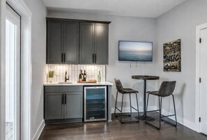A modern kitchen with dark cabinets, a built-in oven, a small refrigerator, and a bar area with two stools.