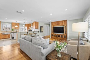 A modern living room with a grey sofa, a coffee table, and a TV mounted on a wooden cabinet. - Home Near Main St / 4BR / Hot Tub / Private Yard (Fredericksburg)