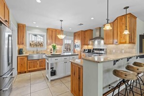 A modern kitchen with wooden cabinets, stainless steel appliances, and a central island with bar stools. - Home Near Main St / 4BR / Hot Tub / Private Yard (Fredericksburg)