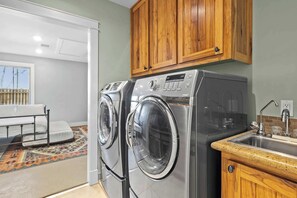 A laundry area with two front-loading washing machines, a sink, and wooden cabinets. - Home Near Main St / 4BR / Hot Tub / Private Yard (Fredericksburg)