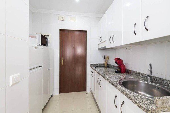 A kitchen with white cabinets, a granite countertop, a red coffee maker, and a stainless steel sink.