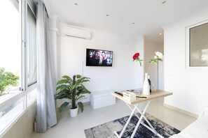 A modern room with a large window, a potted plant, a small table with a vase, and a mounted TV. - Gala de SteraM Flats Torremolinos (Torremolinos)