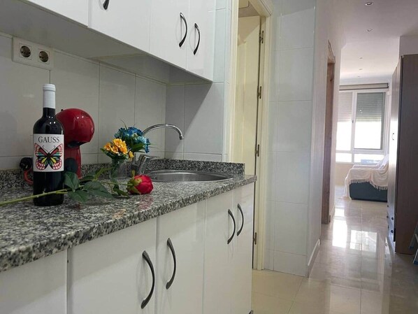 Cozinha com armários brancos, bancada de granito, uma garrafa de vinho e um vaso com flores.