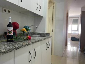 A kitchen with white cabinets, a granite countertop, a wine bottle, and a vase with flowers.