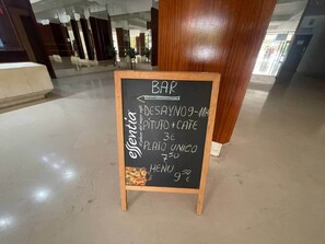 Quadro negro em espaço público anunciando um bar, uma sobremesa e um menu com preços.