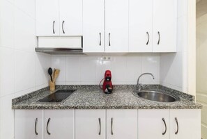 A kitchen with white cabinets, a granite countertop, a red coffee maker, a stove, and a sink. - Gala de SteraM Flats Torremolinos (Torremolinos)