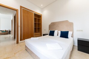 A hotel room with a large bed, a wooden wardrobe, a nightstand, and a small table. - Garden Bay Appart-hotel (Soualem Trifiya)