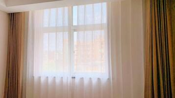 A room with a large window covered by sheer white curtains and two draped brown curtains.