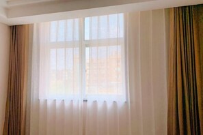 A room with a large window covered by sheer white curtains and two draped brown curtains. - Hangzhou Huiyu Hotel (Hangzhou)